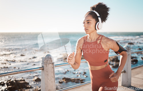 Image of Black woman, fitness and running with headphones at the beach on sea point in Cape Town for exercise. Sporty African American female runner by the ocean coast having a run for cardio training workout