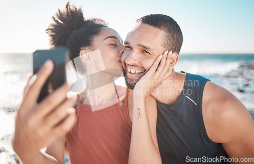 Image of Selfie kiss, fitness and couple with a phone for streaming, training and love at the beach in Bali. Gratitude, exercise and affectionate man and woman with a smile for a mobile photo after a workout