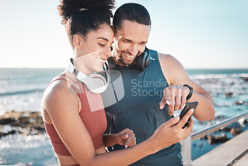 Image of Fitness, couple and phone with smile for social media, communication or discussion relaxing by the beach. Happy man and woman smiling in happiness looking or browsing on smartphone by the ocean coast
