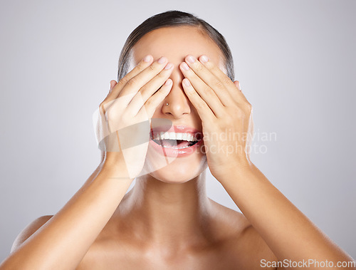 Image of Woman, hands and covering eyes with smile in satisfaction for skincare, cosmetics or beauty against a grey studio background. Happy female model smiling with covered face for makeup surprise