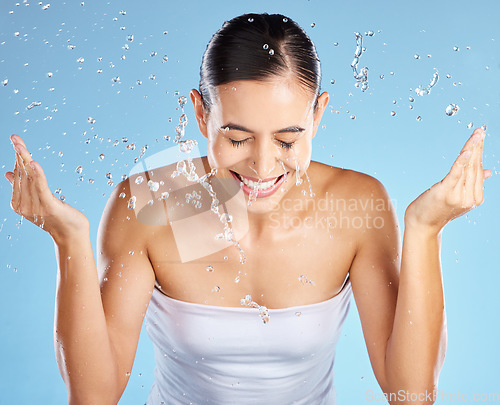 Image of Water splash, skincare and woman isolated on blue background for beauty, cosmetics cleaning and happy. Smile of person or model washing face for dermatology, facial wellness and aesthetic in studio