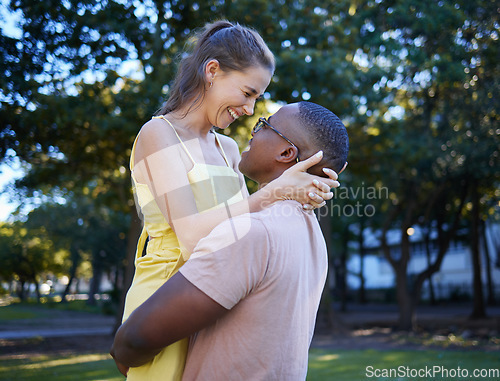 Image of Love, hug and interracial couple at a park, happy and excited against a tree background. Romance, sweet and black man lifting his girlfriend, in love and cheerful in a forest, together and joy