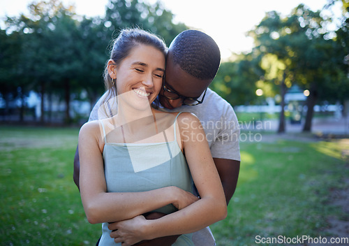 Image of Happy interracial couple, hug and smile for romance, love or care or together in a nature park. Woman smiling with man hugging her for relationship embrace, support or trust kissing shoulder outside