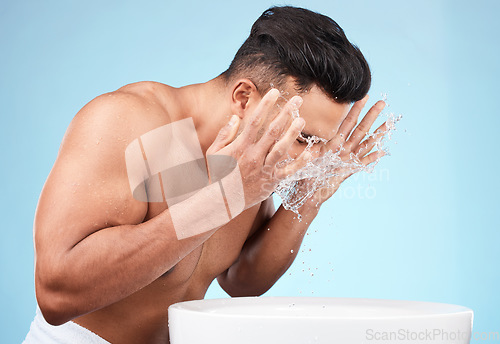 Image of Clean, grooming and man washing face with water for skincare, morning hygiene and care of body on a blue studio background. Beauty, wellness and model with a facial water splash for cleaning