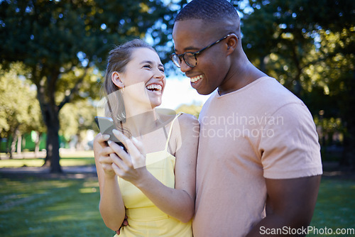 Image of Interracial, social media and couple with a phone in nature, funny communication and laughing at meme. Comic, streaming and black man and woman reading a joke on a mobile in a park in France