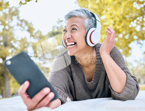Image of Music, headphones and senior woman with phone at park streaming radio or podcast. Thinking, cellphone and happy, elderly and female in retirement enjoying audio while laughing at comic meme.