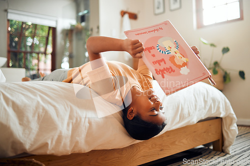 Image of Happy child reading book on bed for home learning, language education and creative development upside down. Smart, intelligent and Indian kid with English story for fun, relax and holiday activity