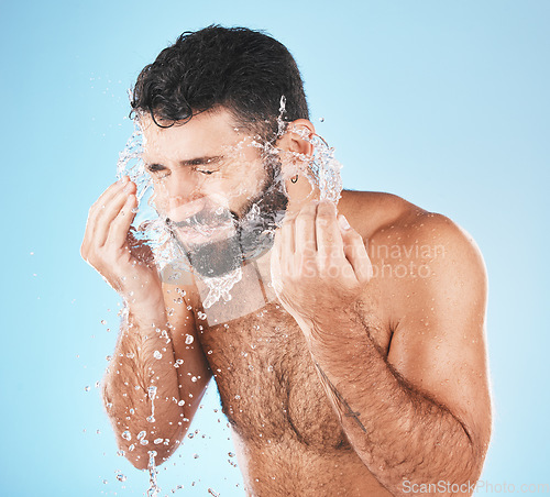 Image of Man, water splash face and cleaning in studio for wellness, health and self care groom by blue background. Model, bathroom and water with hands for healthy facial, self love and cosmetics by backdrop