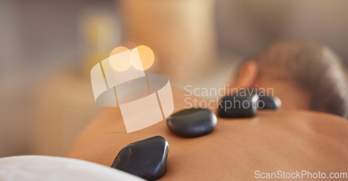 Image of Spa, man and stone massage to relax, luxury and health for body care, peace and holistic care. Male, gentleman and lying on table at resort, rocks and wellness therapy for skincare and stress relief.