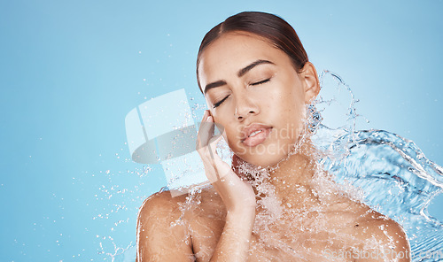 Image of Woman, hand and water splash for face skincare, dermatology wellness or Brazilian healthcare grooming on blue background studio. Beauty model, water drop or facial cleaning in wet hygiene maintenance