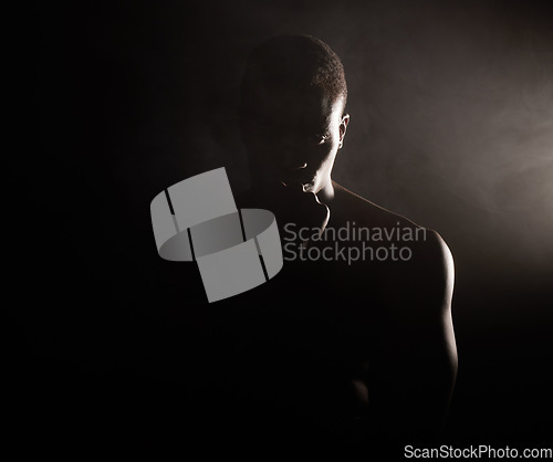 Image of A handsome, muscular young african american man in studio against a dark background. A macho male athlete looking thoughtful isolated on black. Exercising body and mind. A question of mental health