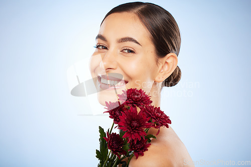 Image of Skincare, flowers and beauty portrait of woman on studio blue background for healthy skincare, wellness and luxury makeup in Spain. Face, smile and model with floral chrysanthemum for natural perfume