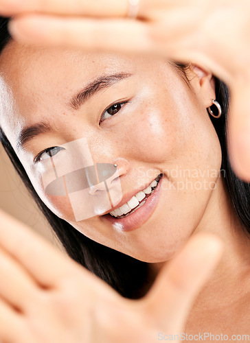 Image of Studio portrait, hand frame and asian woman with smile for skincare, natural skin glow and wellness. Happy Japanese model, cosmetic beauty and healthy aesthetic with self care dermatology headshot