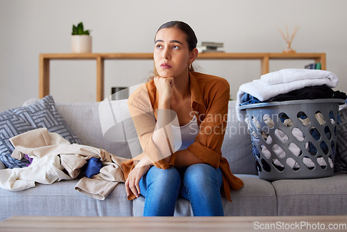 Image of Laundry, bored and break with a woman cleaner sitting on a sofa in her living room at home for spring cleaning. Depression, cleaning and laundry basket with a female housekeeper resting on a couch