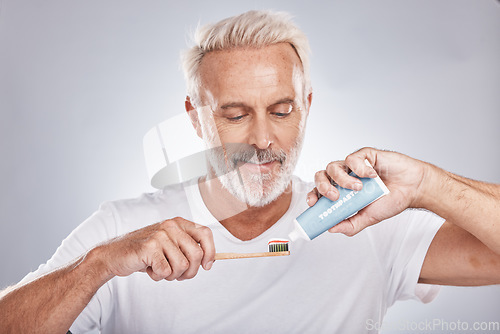 Image of Face, toothpaste and senior man with toothbrush in studio isolated on a gray background. Hygiene, cleaning and elderly male model holding product for brushing teeth, dental wellness and healthy gums.