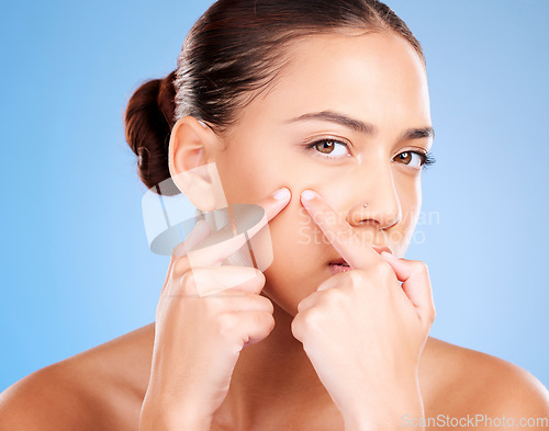 Image of Woman, face and squeeze pimples, acne and facial scar on studio blue background. Portrait of young female model worried for skincare problem, aesthetic beauty cosmetics and pop blackhead with fingers