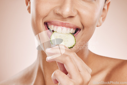 Image of Hand, mouth and cucumber with a model black woman biting a vegetable in studio on a beige background. Health, beauty and skincare with a young female eating a slice of veg for natural wellness