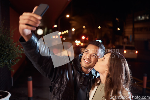 Image of People, phone and night selfie kiss on cheek on city street, social media or profile picture in birthday celebration vlog. Happy smile, bonding or couple of friends on mobile photography tech in dark