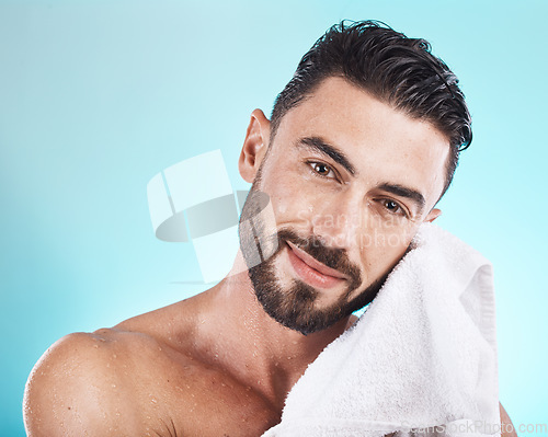 Image of Man face, towel and skincare while wet after a shower, facial or bath for skincare, hygiene and dermatology on blue. Portrait of happy male model in studio for clean body for health and wellness
