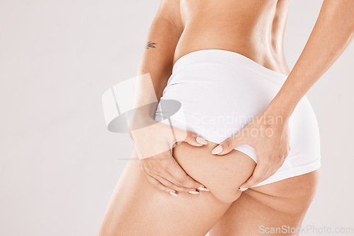 Image of Hands, butt and underwear with a woman model in studio on a gray background squeezing cellulite from the back. Liposuction, wellness and heath with a female touching her buttocks or ass in panties