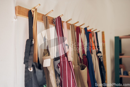 Image of Clothing rack, apron and workshop of clothes hanging on a creative studio wall for art, style or design. Closeup of aprons or work equipment for artistic development on rack for business startup