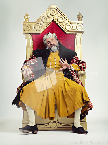 Image of King, royalty and bored man on throne in studio isolated on gray background. Monarch, medieval royal and annoyed senior male, leader or frustrated ruler, looking at hand and sitting on golden seat.