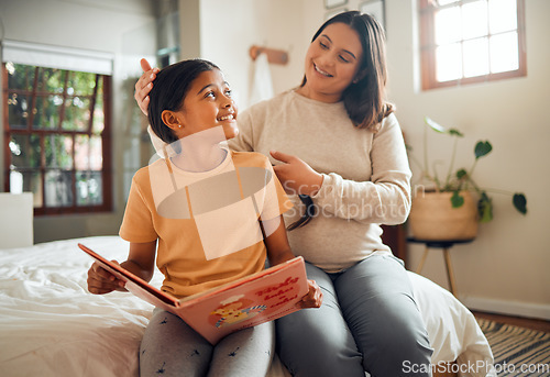 Image of Family, book or learning and a girl reading in a bedroom with her mom playing with her hair in their home. Books, education and love with a mother and daughter bonding while sitting on a bed together