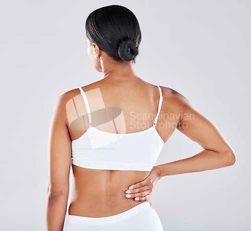 Image of Back, body and pain with a model black woman holding her side in studio on a gray background while suffering from injury. Medical, health and anatomy with a female in underwear rubbing her muscle