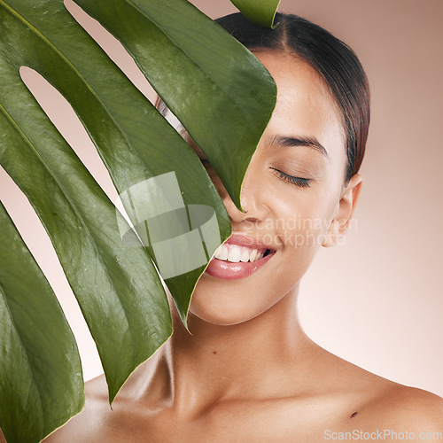 Image of Black woman, smile and leaf with beauty, studio and cosmetic wellness with smile, face glow and makeup. Model, skin health and facial cosmetics, self care and aesthetic with leaves by studio backdrop