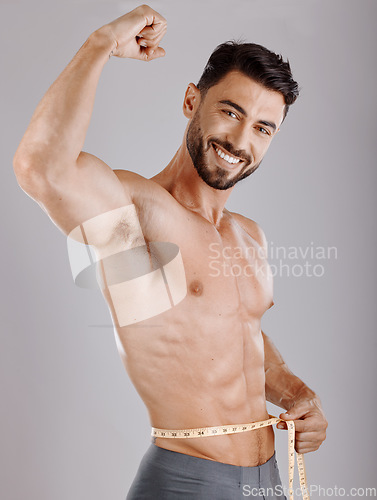 Image of Portrait, body and weightloss with a man measuring his waist in studio on a gray background for diet progress. Fitness, heath and wellness with a topless male model flexing his strong bicep muscle