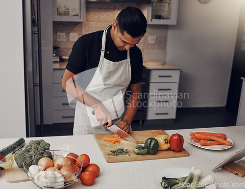 Image of Cooking, food and vegetables with a man cutting ingredients in the kitchen on a wooden chopping board. Salad, health and diet with a male chef preparing a meal while standing alone in his home