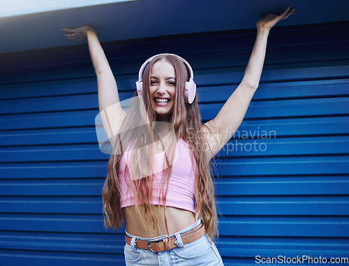 Image of Portrait, music or freedom with a woman on a blue background standing arms raised in celebration for fun. Party, fashion and headphones with an attractive young female streaming or listening to audio