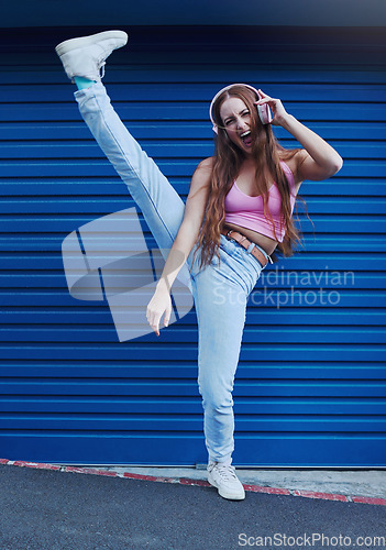 Image of Crazy music, freedom and excited girl on blue background in city listening to track and audio on headphones. Fashion, lifestyle and woman with leg up for dance, happy attitude or streaming song