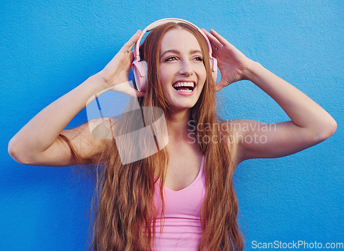 Image of Music, headphones and blue background with a woman streaming or listening to audio for fun. Radio, internet and 5g with an attractive young female using wireless technology to listen to a song