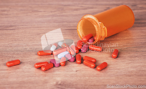 Image of Pills, medicine and suicide with a tablet container on a wooden table or surface for drug addiction and overdose. Health, medication and pharmacy with prescription tablets spilled from above