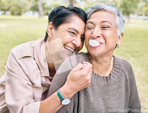 Image of Senior women, friends and hug in park for comic, funny and happy time together in nature with bubblegum. Old woman, embrace and laughing for memory, joke or bubble by trees, nature or forest to relax