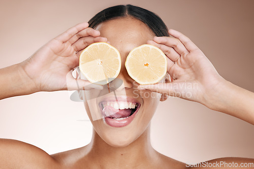 Image of Woman face, tongue and lemon skincare hands on studio background in organic dermatology routine and healthcare wellness. Zoom, happy and fun beauty model and facial fruit, diet food and eyes product