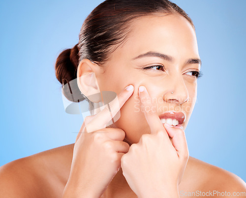 Image of Skincare, beauty and woman squeeze pimple before a natural cosmetic face treatment in a studio. Acne, cosmetics and female model pop blackheads or facial scar with her fingers by a blue background.