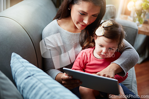 Image of Family, baby and tablet with a mother and daughter sitting on a sofa in the living room of their home for development. Kids, education or overhead with a woman and girl child learning in a house