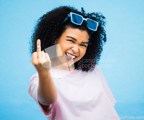 Image of Portrait, middle finger and hand, emoji and black woman in studio, rude and carefree on a blue background. Face, rebel and hands by girl for message, attitude and expression, personality and isolated