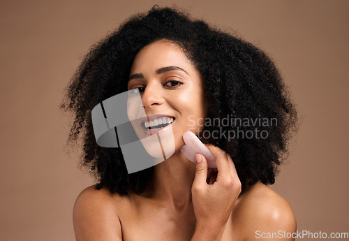 Image of Face portrait, skincare and black woman with gua sha in studio isolated on a brown background. Makeup, cosmetics and happy female model holding jade stone for anti aging, facial treatment or massage.