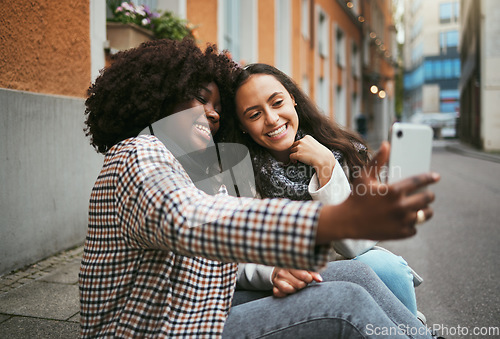 Image of City, friends and women take selfie with phone and sitting on sidewalk laughing and happy together. Photo, video call and black woman with girl friend with urban fun and social media profile picture.