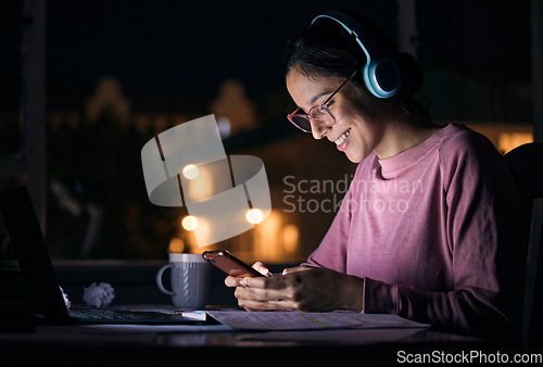 Image of Phone, night and woman networking with headphones while listening to music, radio or podcast. Happy, smile and girl browsing social media, mobile app or internet with cellphone at a desk in her home.