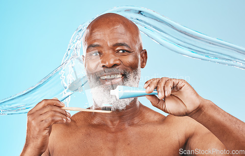 Image of Water splash, oral hygiene and portrait of a man in a studio for mouth health and wellness. Toothpaste, toothbrush and elderly African guy brushing his teeth for fresh dental care by blue background.