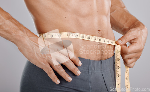 Image of Man, body and tape measure on waist in studio on gray background. Health, fitness and male model with measuring tape for abdomen to track exercise training results, muscle goals or weight loss target