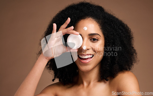 Image of Face, skincare and black woman with cream container in studio on a brown background. Makeup cosmetics, portrait and female model apply facial lotion, product or moisturizer creme for healthy skin.