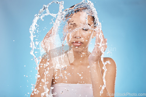 Image of Woman, hands and water splash for washing face grooming, healthcare wellness or self care hygiene on studio blue background. Beauty model, water drops cleaning and facial skincare in Brazil bathroom