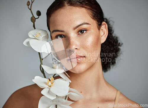 Image of Skincare, face portrait and woman with orchid in studio isolated on a gray background. Floral makeup, organic cosmetics and female model with flowers for healthy skin treatment, wellness and beauty.