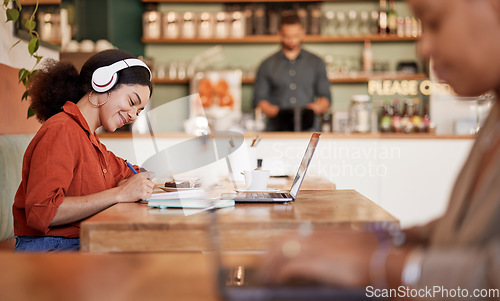 Image of Woman, student and studying in cafe, laptop and make notes for exams, smile and concentration for test. Young female, lady or academic with headphones, podcast or writing audio to text in coffee shop