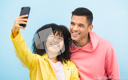 Image of Friends, phone and face with smile for selfie on a blue background for fashion, style or friendship together. Young man and woman smiling in happiness looking at smartphone for happy photo moments